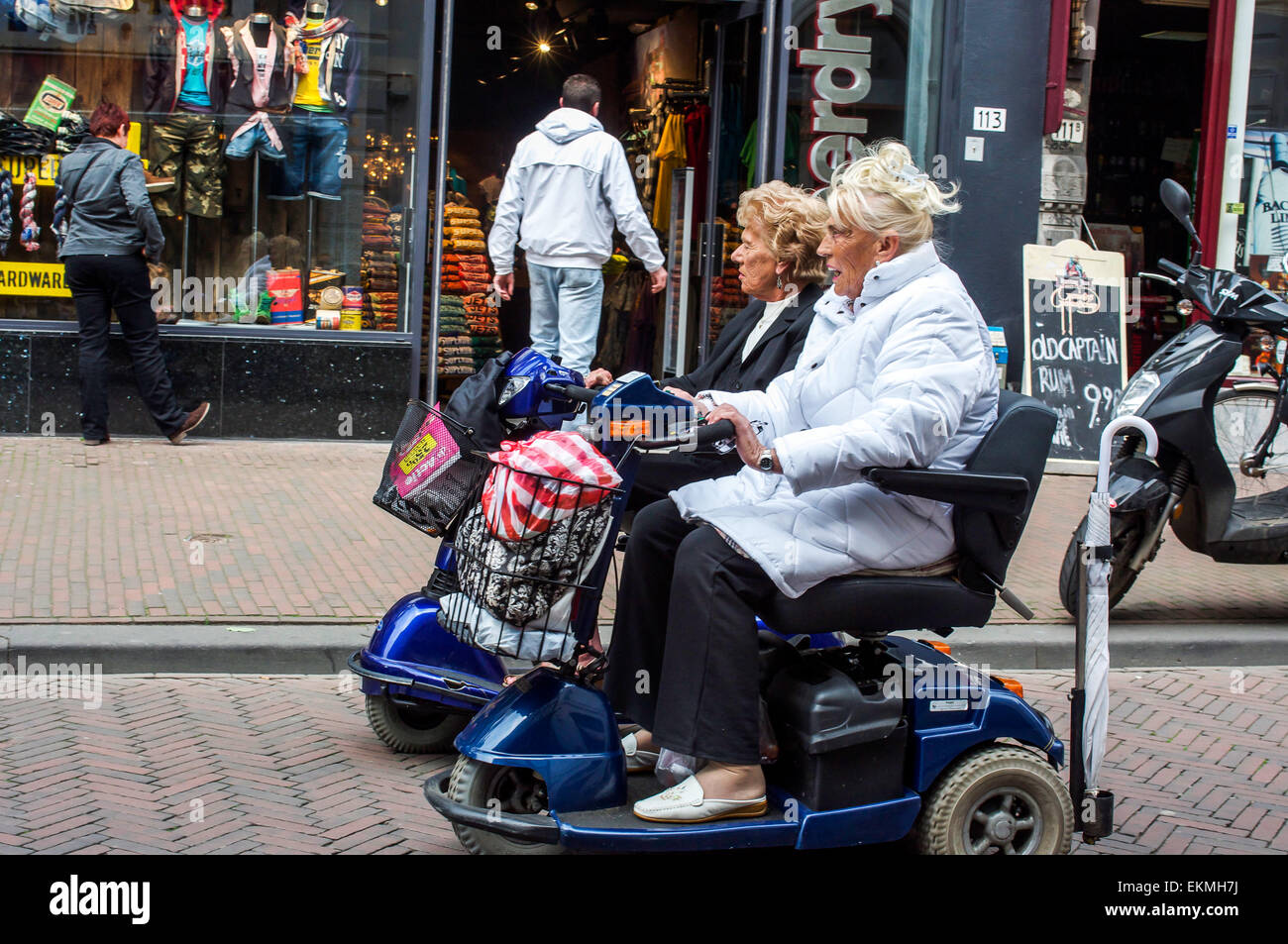 Elderly zooming grannies on mobility scooters ride rather quickly through pedestrian shopping street in Rotterdam, Netherlands. Stock Photo