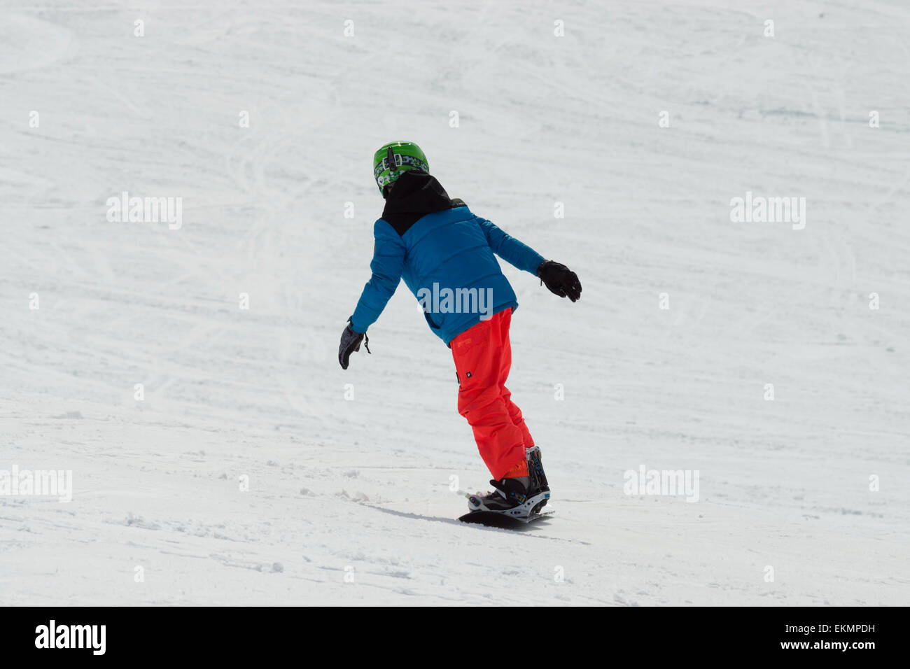 A smooth child snowboarder, is speeding down the alps while turning left to keep the momentum going. Stock Photo