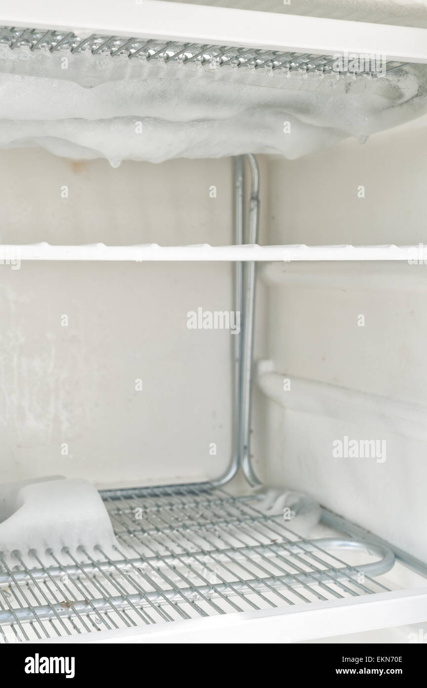 time to defrost an ice laden inefficient deep freezer with built up layers of ice  frozen water on the elements and shelf inside Stock Photo