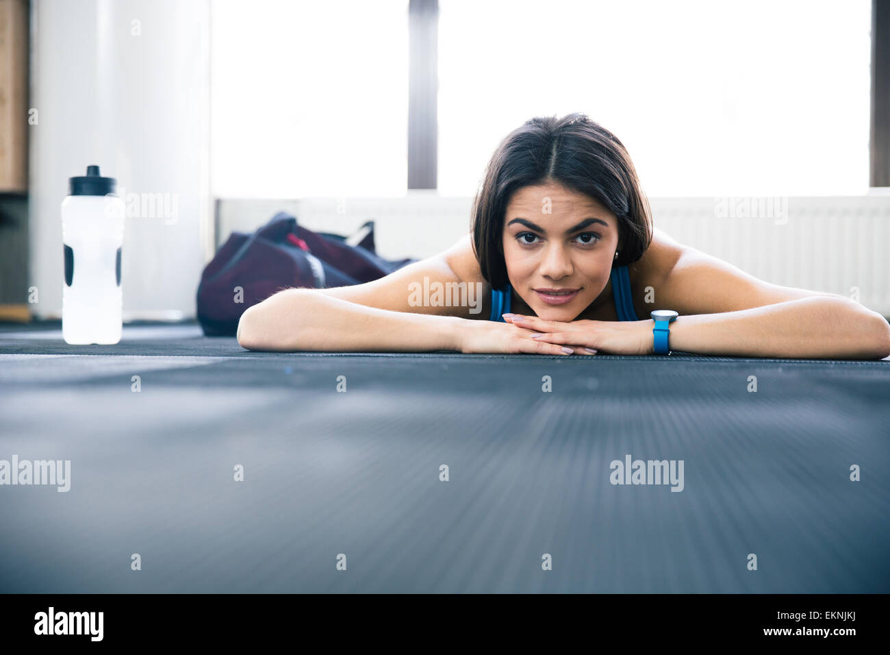 Cute young sportive woman lying on the floor at gym. Looking at camera ...