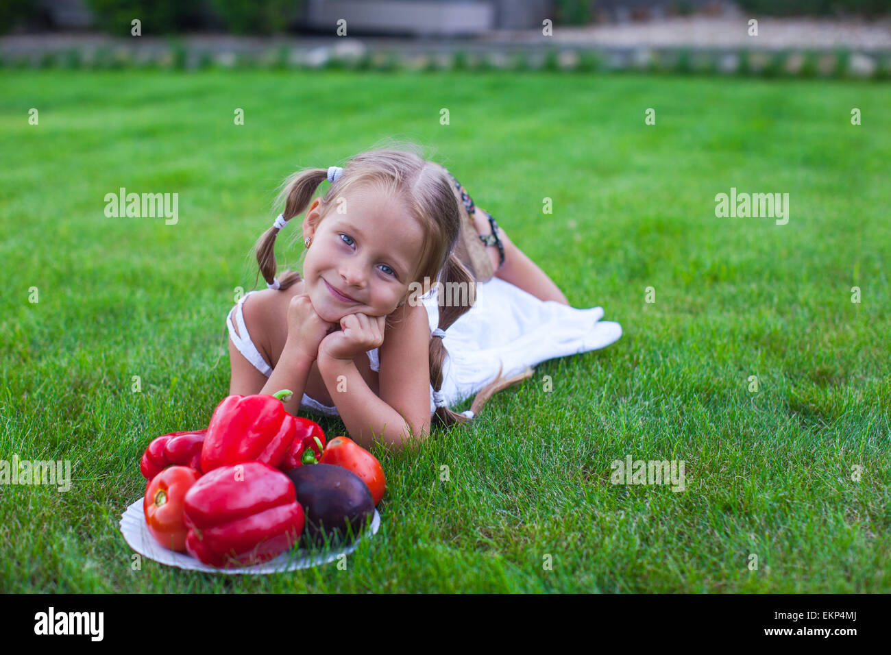 Lovely girl with pigtails in a garden with a plate of vegetables Stock Photo
