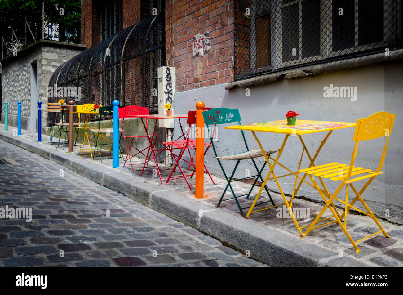 A row of colourful tables and chairs on a cobbled sidewalk in Paris