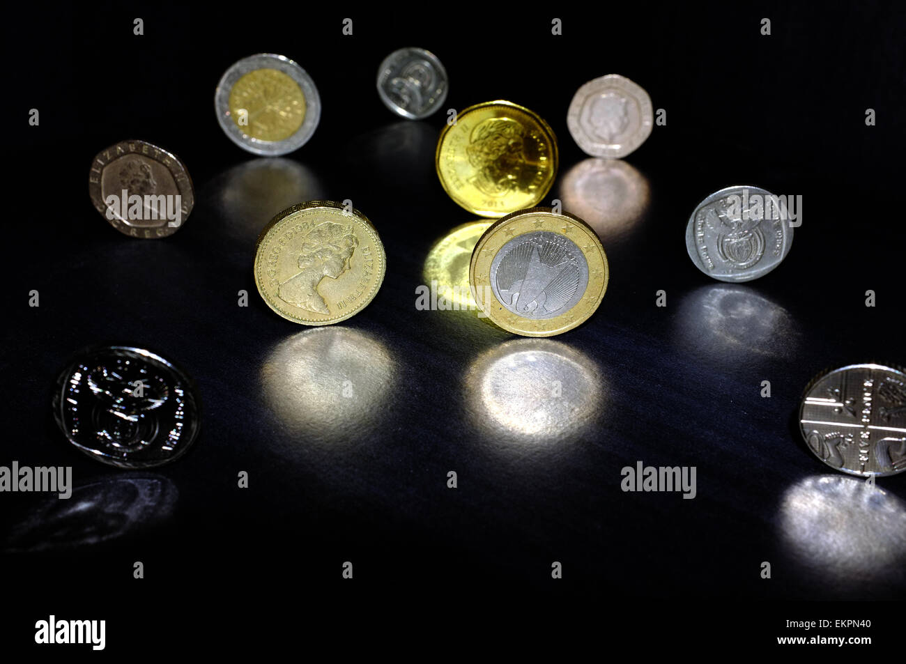 Coins from different currencies reflected on a black surface. Stock Photo