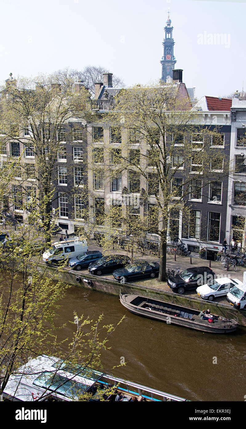 Central Amsterdam showing parked cars bikes and housing along the canal with Westerkerk Church Tower in the background. Stock Photo