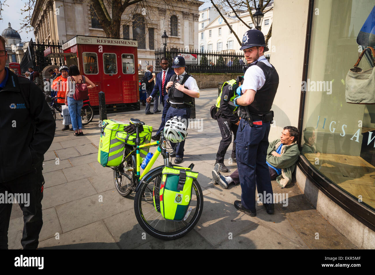 Two london policemen help a London Ambulance Cycle Responder attend to a man Stock Photo