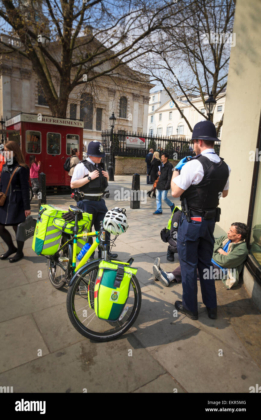 Two london policemen help a London Ambulance Cycle Responder attend to a man Stock Photo