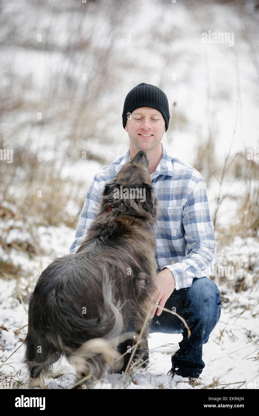 A man in a checked shirt greeting and patting a dog. Stock Photo