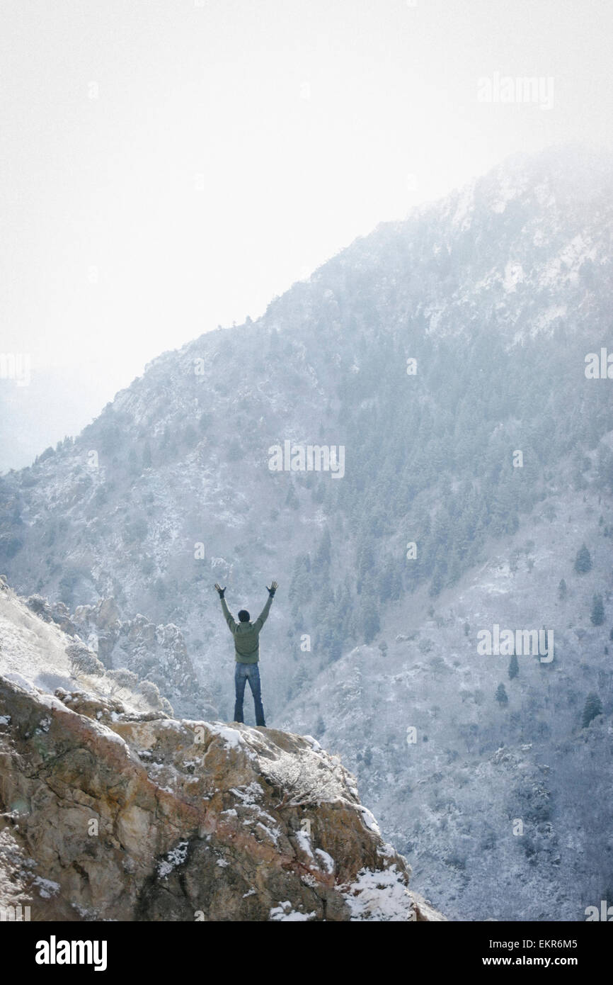 A man greeting the sun, with his arms raised on a rock outcrop in the mountains. Stock Photo