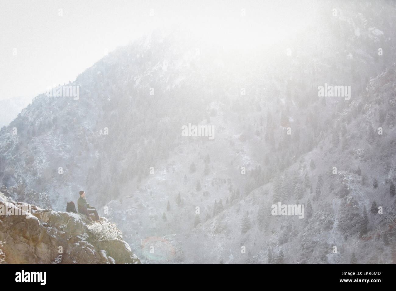 A man, a hiker in the mountains, taking a rest on a rock outcrop above a valley. Stock Photo