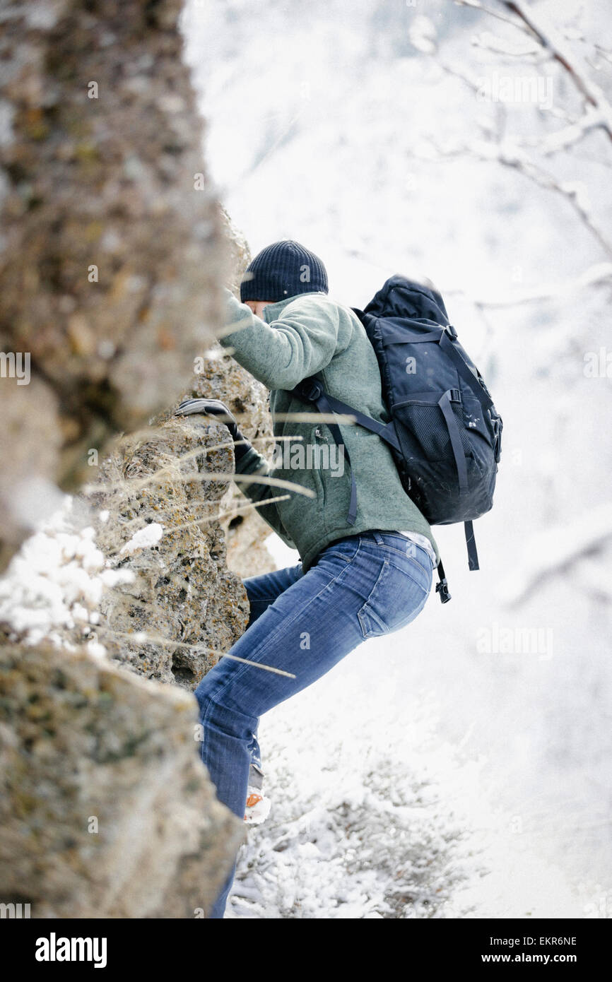 A man wearing a fleece jacket and hat, carrying a rucksack, climbing up a rocky cliff face. Stock Photo