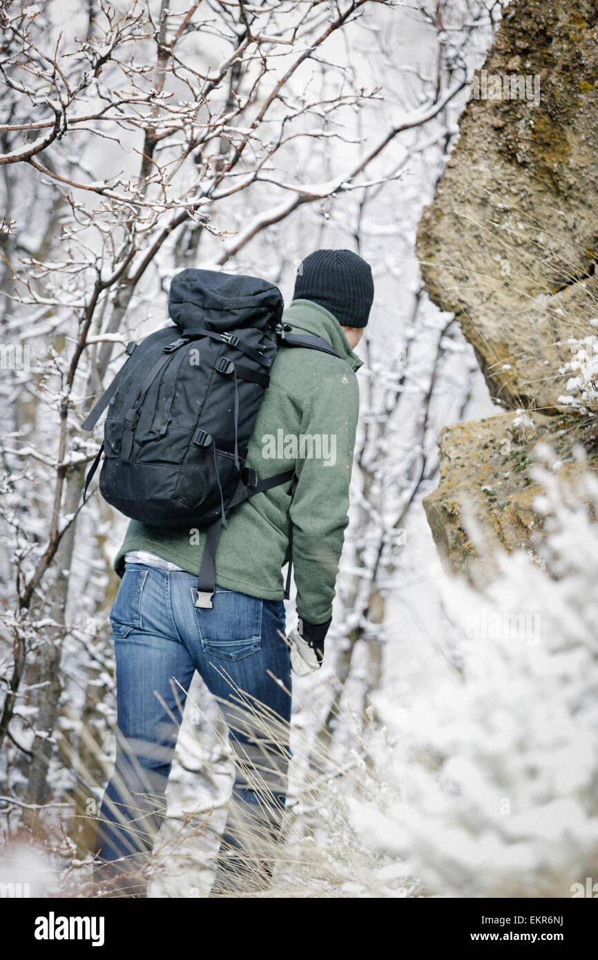 A man wearing a fleece jacket and hat, carrying a rucksack, climbing up a rocky slope. Stock Photo