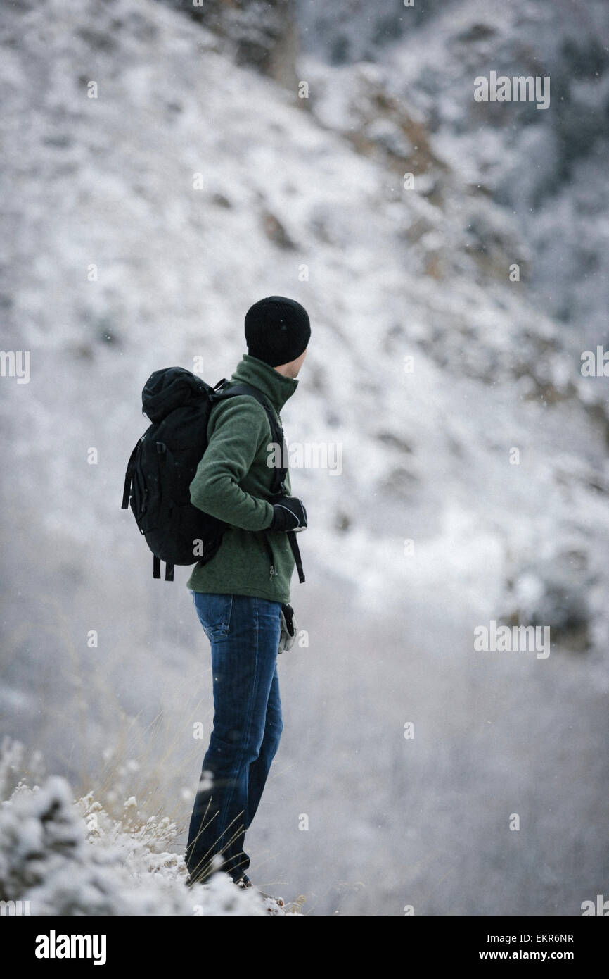 A man wearing a fleece jacket and hat, carrying a rucksack, on a mountain slope. Stock Photo