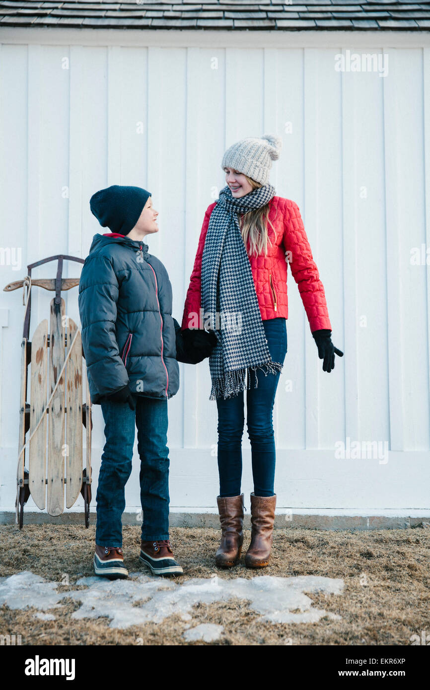 Two children, brother and sister, standing side by side in winter coats in a yard. Stock Photo