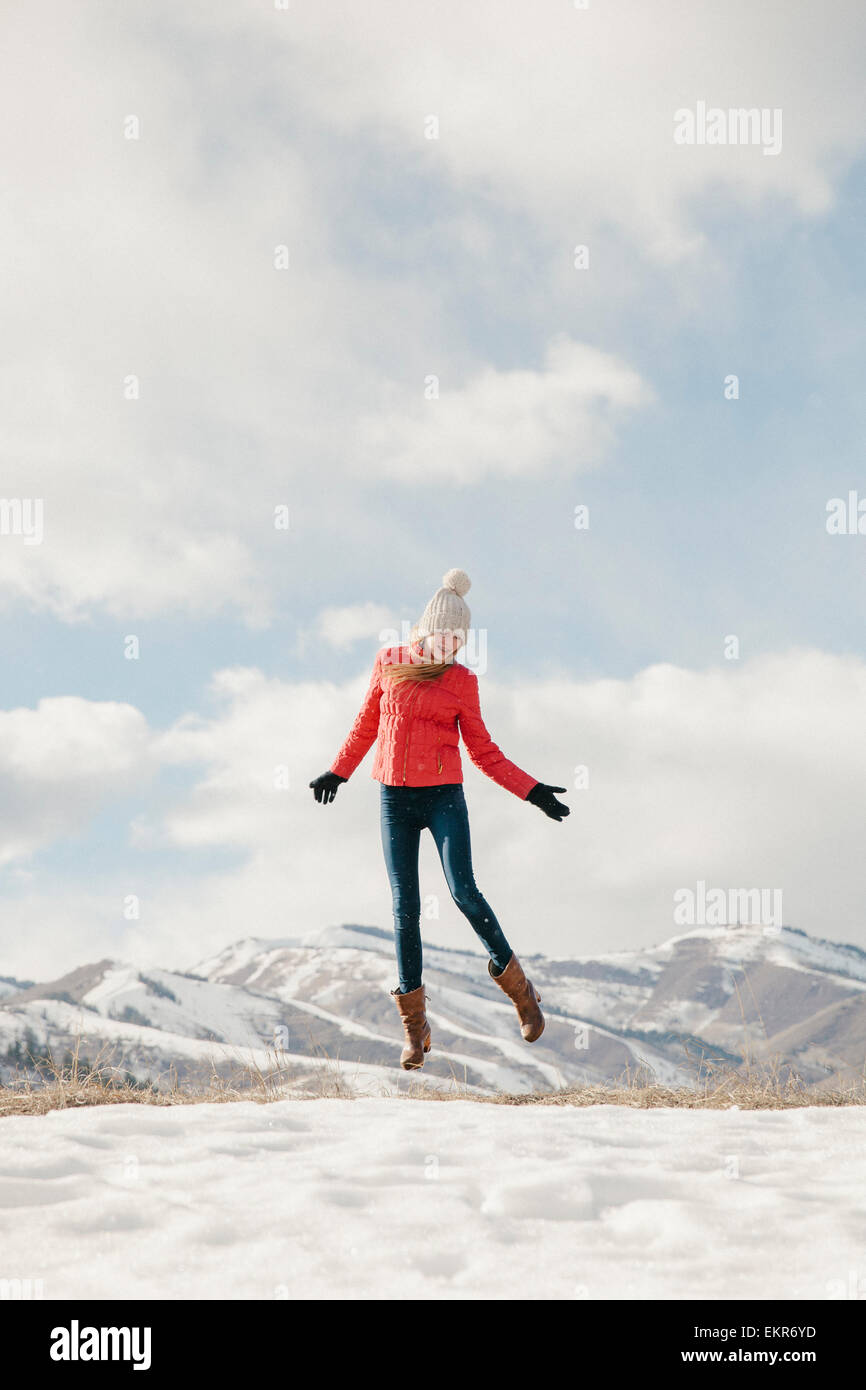 A young girl with long legs and red jacket, leaping in the air above the snow Stock Photo