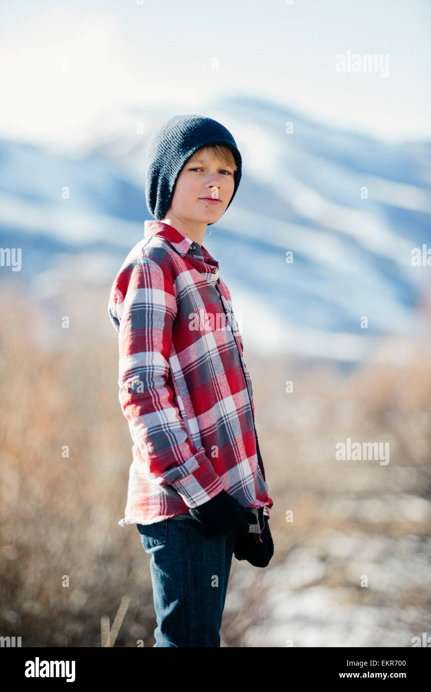 A boy with a woolly hat and checked shirt standing in open countryside in winter. Stock Photo
