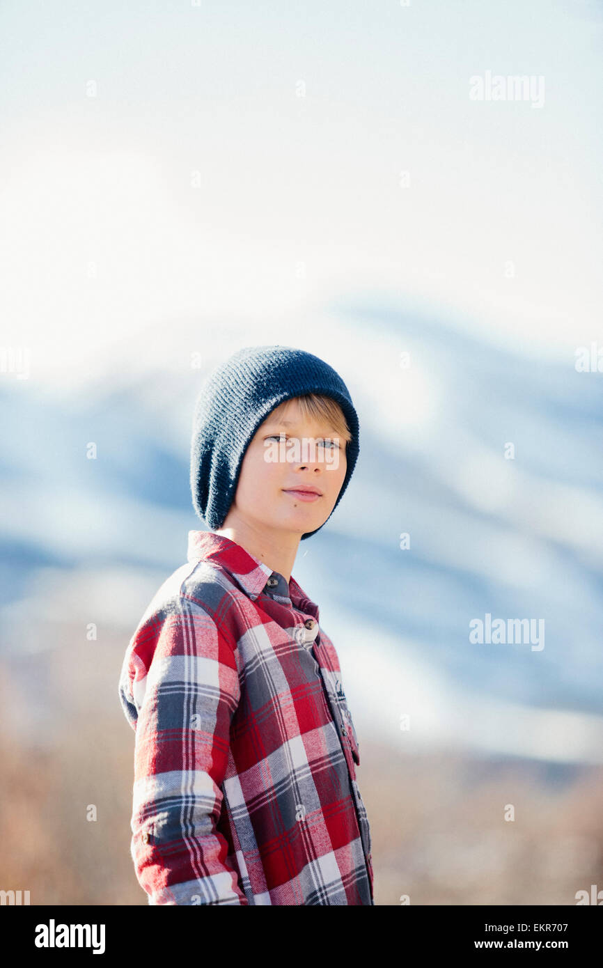 A boy with a woolly hat and checked shirt standing in open countryside in winter. Stock Photo