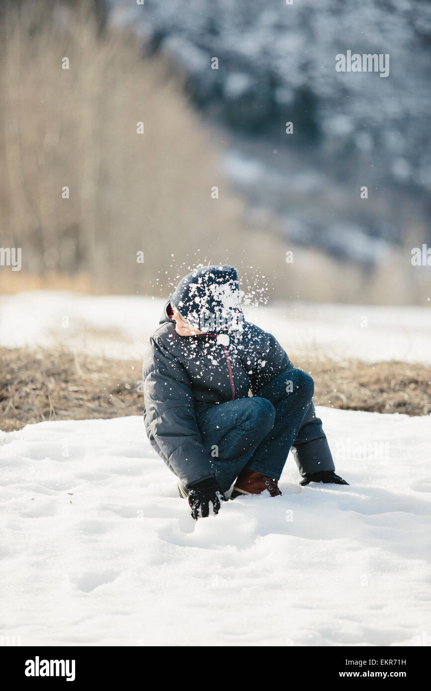 A boy in a blue coat and woolly hat turning his head from a snowball which has hit him. Stock Photo