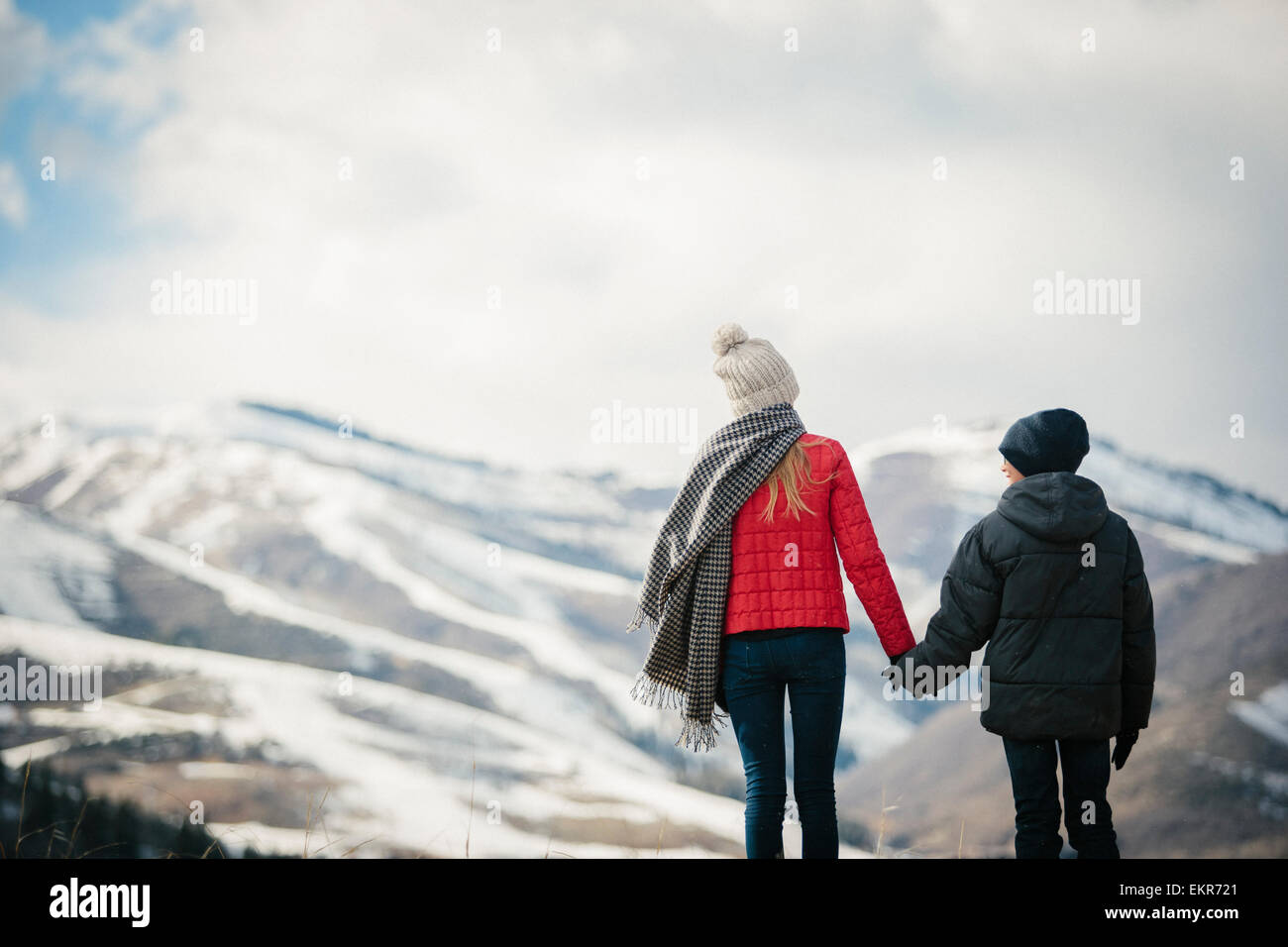 A brother and sister standing side by side in the snow, back view. Stock Photo