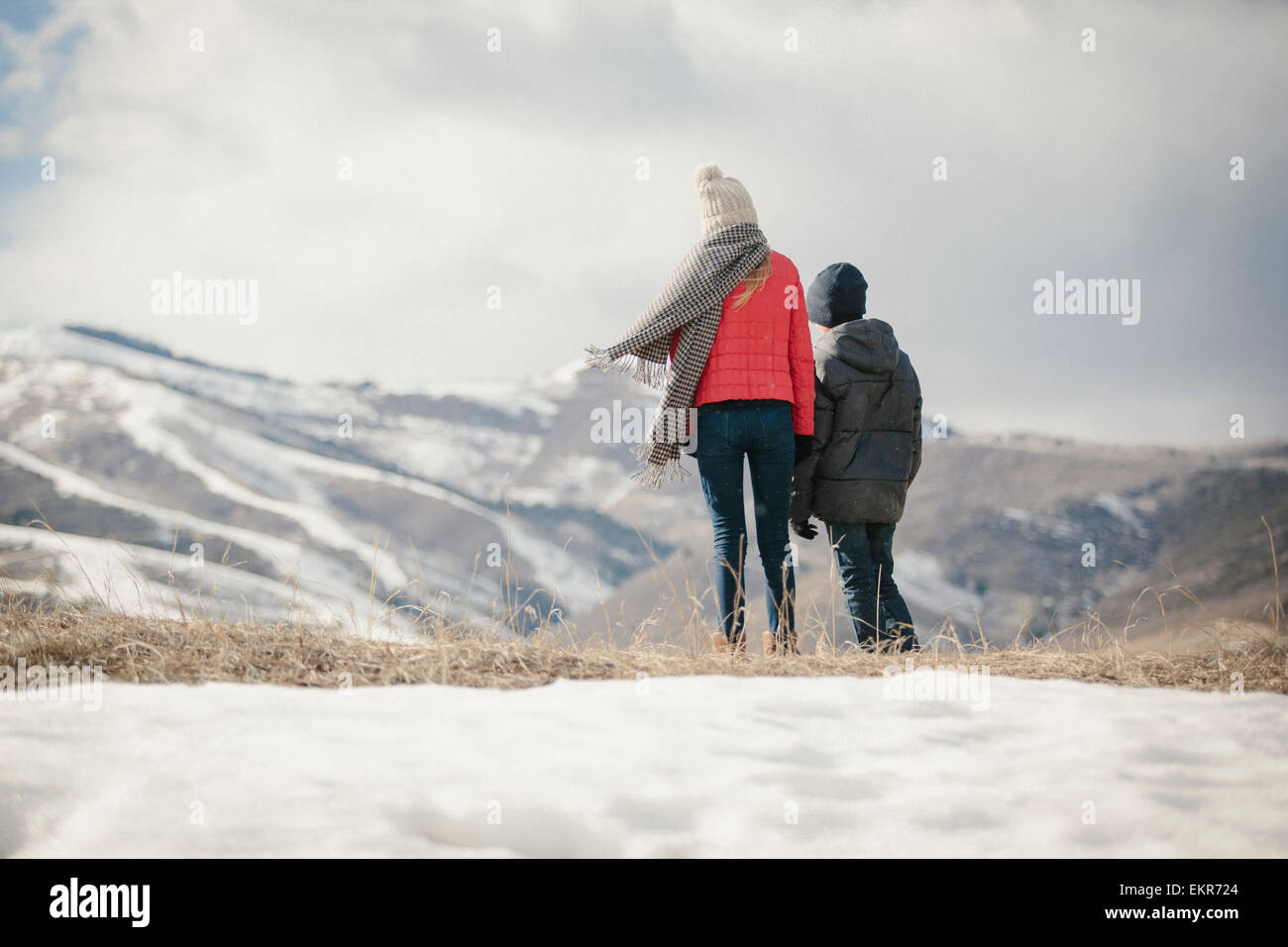 A brother and sister standing side by side in the snow, back view. Stock Photo