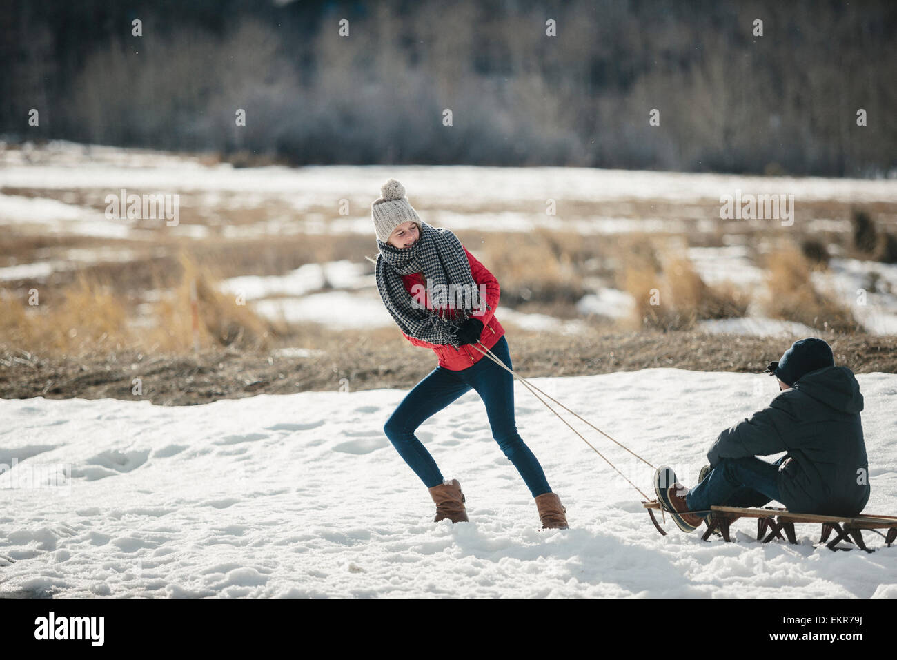 A brother and sister in the snow, one pulling the other on a sledge. Stock Photo
