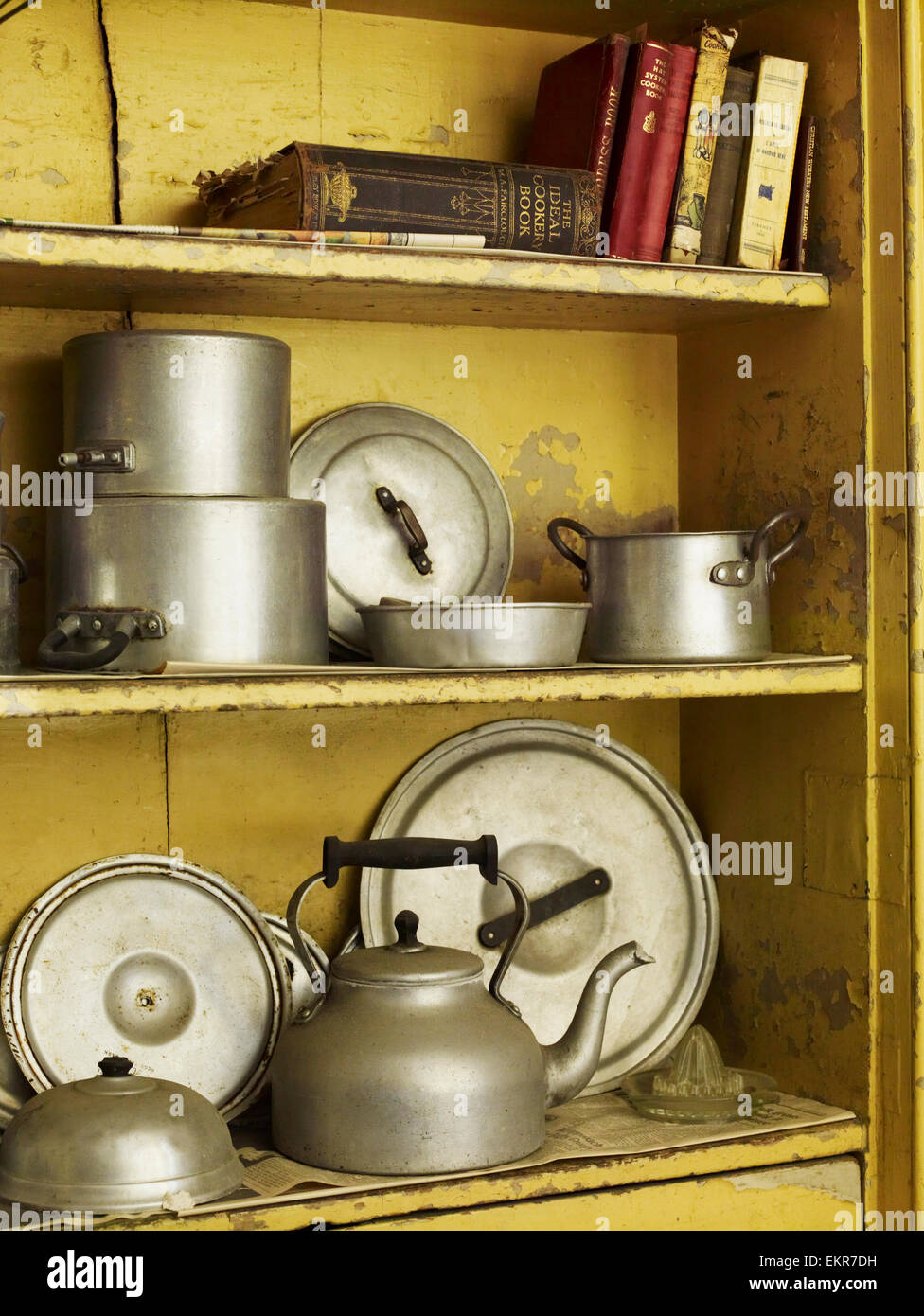 Old well worn recipe books and pots and pans on a kitchen shelf. Stock Photo