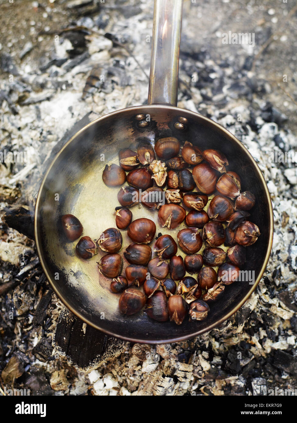 A frying pan over an open fire, with blackened fresh roasted chestnuts