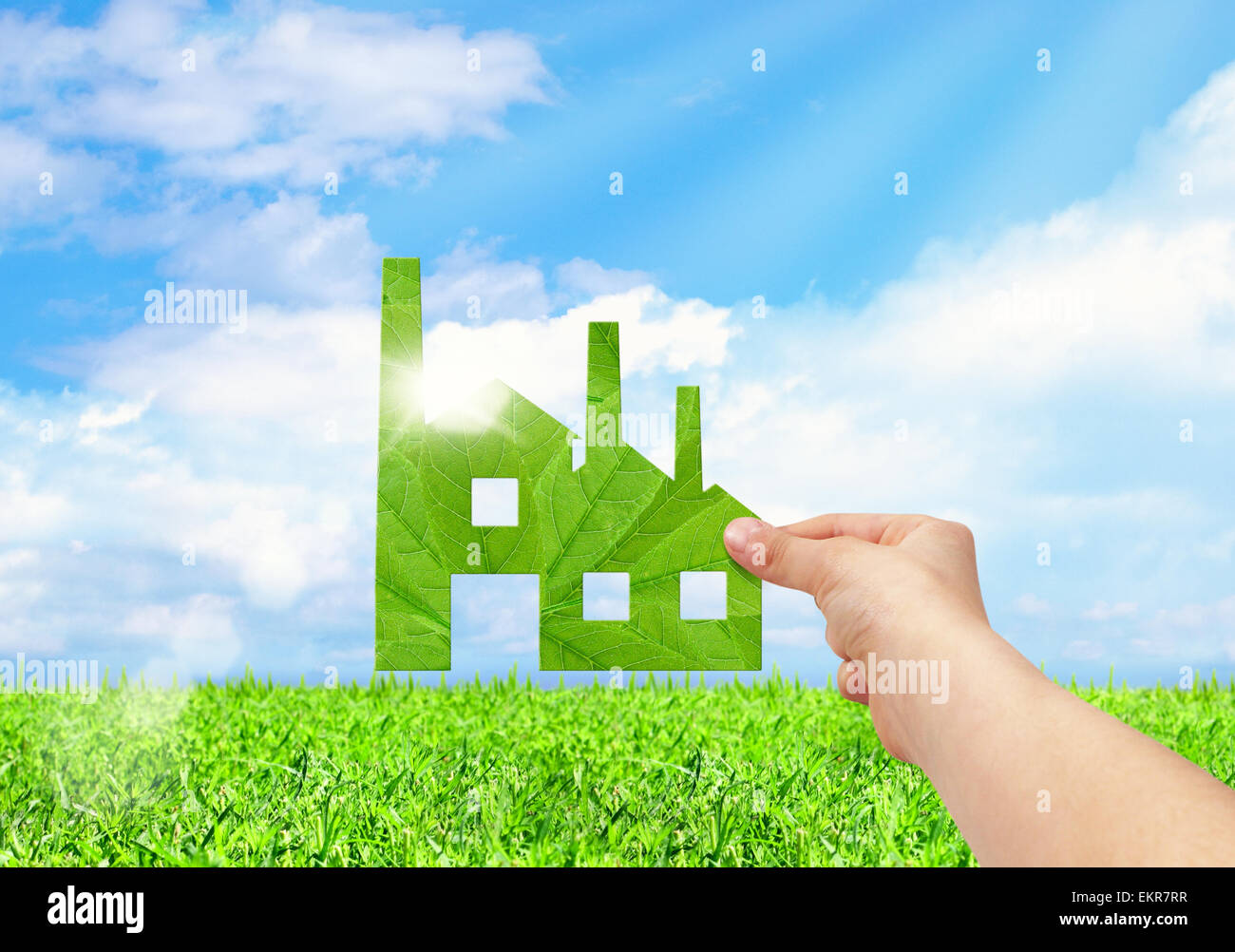 Hand hold factory icon on field and blue sky background, Eco green factory concept Stock Photo