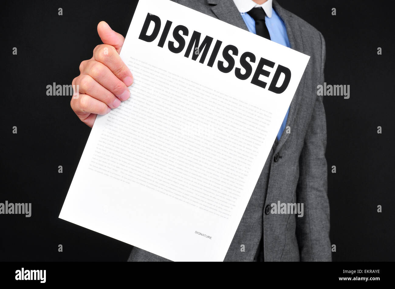 a young caucasian man in gray suit showing a document with the text dismissal written in it on a black background Stock Photo