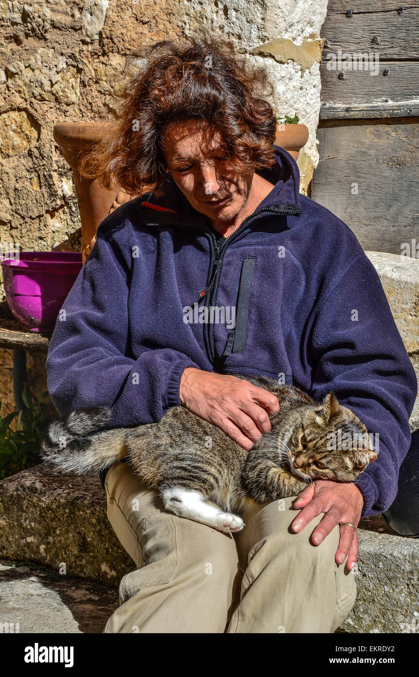 woman sitting on the steps of stone stairs stroking a brown speckled cat snuggling on her lap Stock Photo