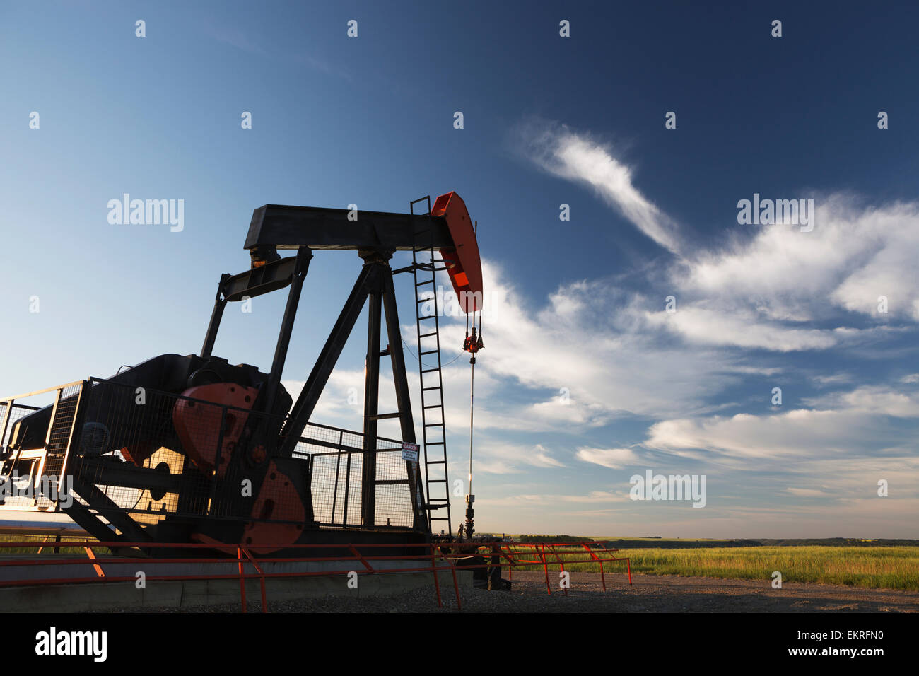 Pump jack at sunrise with colourful clouds and blue sky in green field