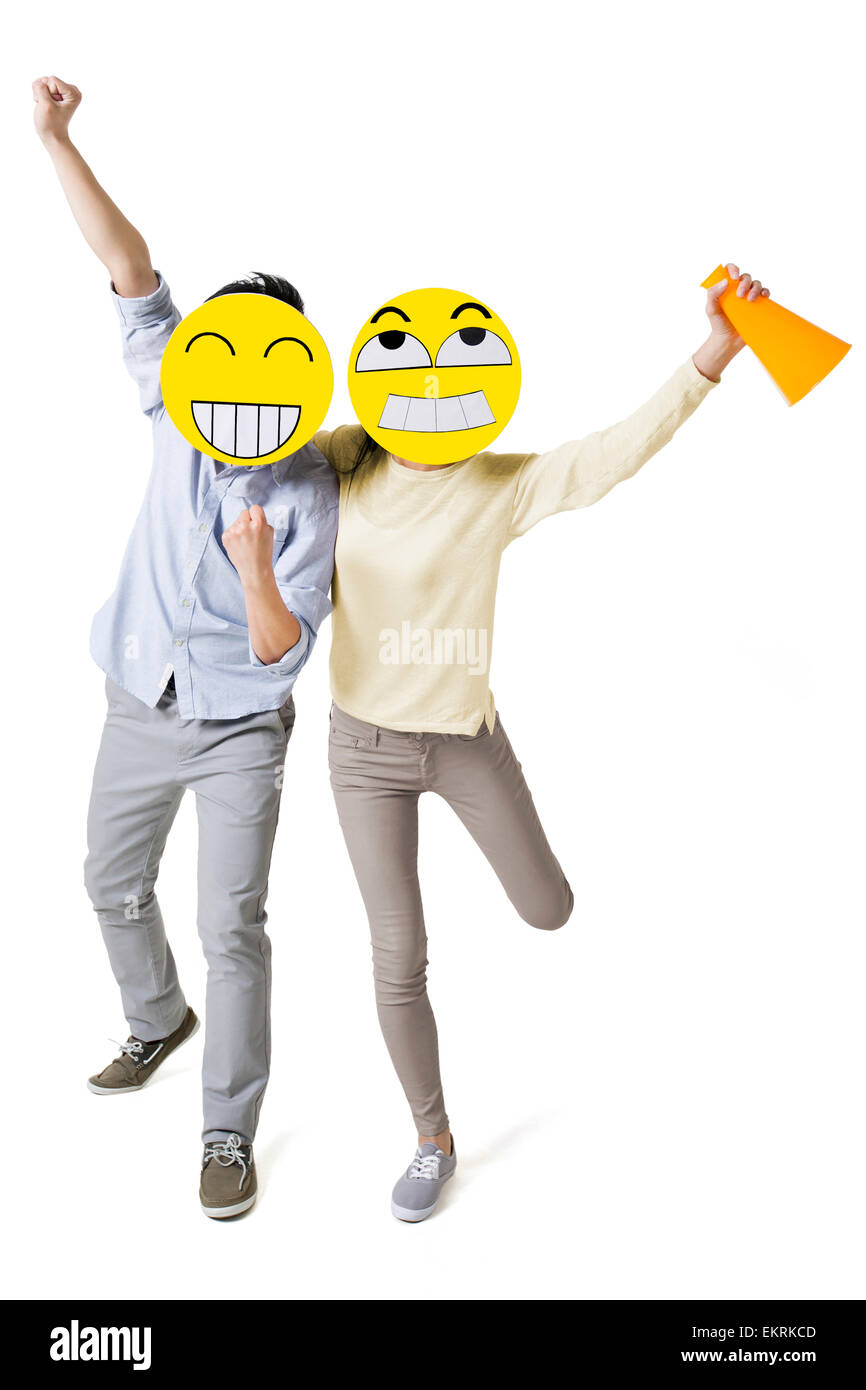 Young couple cheering with two happy emoticon faces in front of their faces Stock Photo