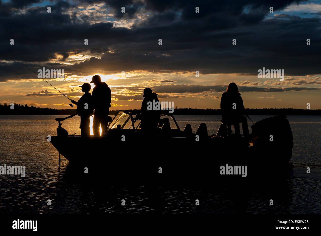 Silhouette of a family fishing from their motorboat on a lake at sunset ...