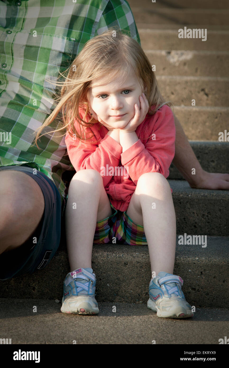 A Young Girl Cradles Her Face In Her Hands As She Sits On A Step Beside