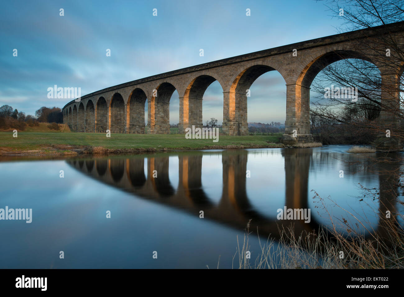 Under bright blue sky, arches of Arthington Viaduct railway bridge are reflected in calm water of the River Wharfe - West Yorkshire, England, UK. Stock Photo