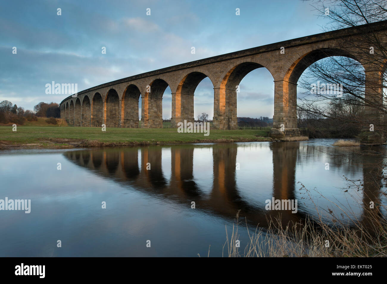 Under bright blue sky, arches of Arthington Viaduct railway bridge are  reflected in calm water of the River Wharfe - West Yorkshire, England, UK. Stock Photo