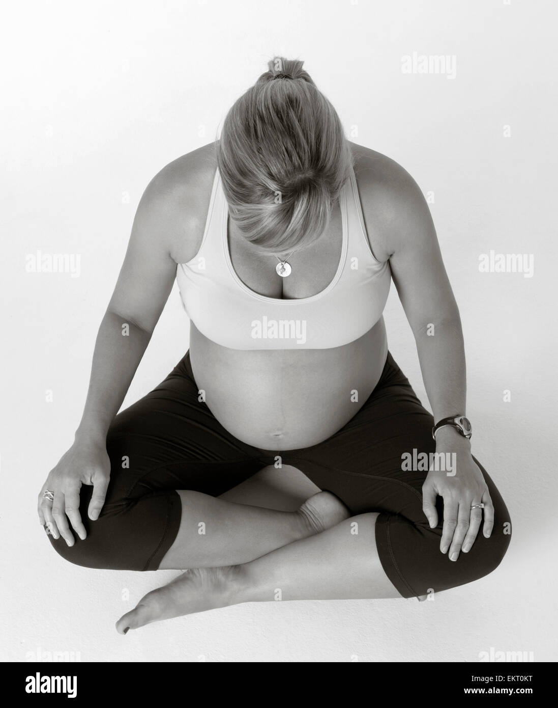Black And White Studio Maternity Shot On White Of Mom Sitting Crossed Legged With Her Head Down Stock Photo