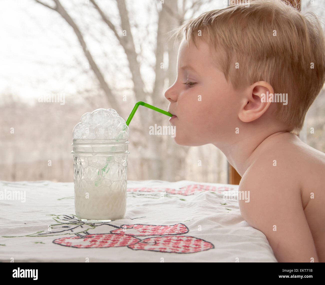 boy blows milk bubbles in his glass Stock Photo
