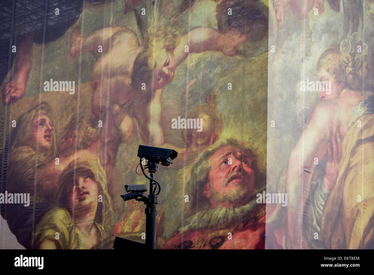 CCTV cameras keep watch on the population, seen in front of a giant construction hoarding in Whitehall, Westminster, London. The illustration is from the Peter Paul Rubens painting 'The Apotheosis of James I' which appears on a ceiling inside the Banqueting House, behind this screen and location of King James' son, Charles 1st execution. Stock Photo