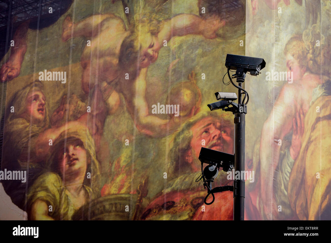 CCTV cameras keep watch on the population, seen in front of a giant construction hoarding in Whitehall, Westminster, London. The illustration is from the Peter Paul Rubens painting 'The Apotheosis of James I' which appears on a ceiling inside the Banqueting House, behind this screen and location of King James' son, Charles 1st execution. Stock Photo