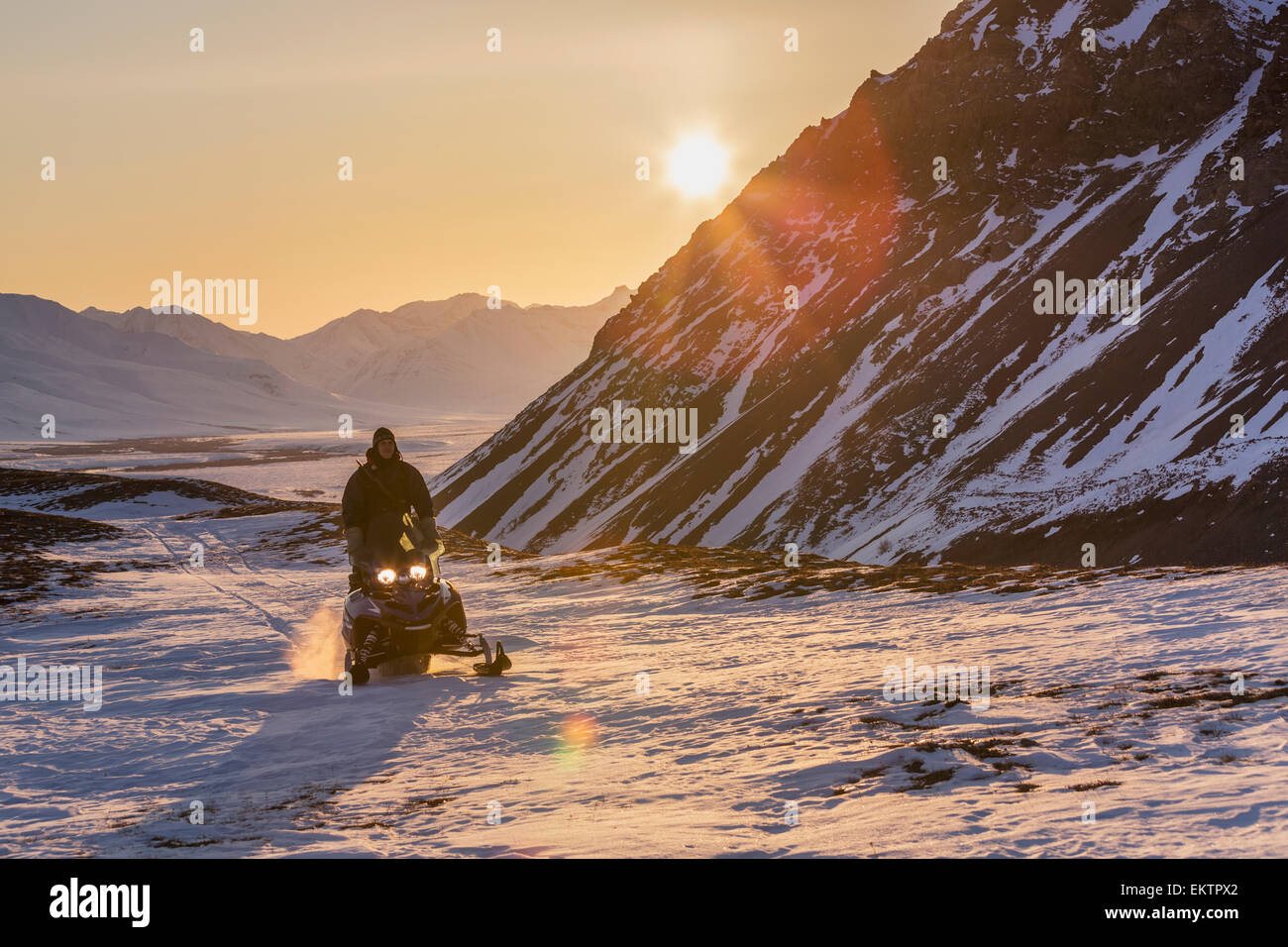 Man riding a snowmachine up the Anaktuvuk River Valley at sunset, Gates