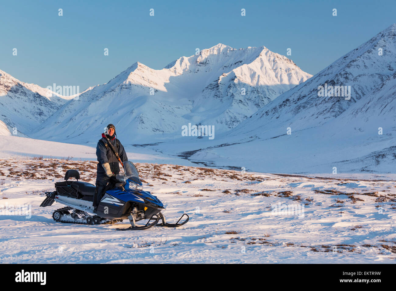 Man riding a snowmachine up the Anaktuvuk River Valley at sunset, Gates