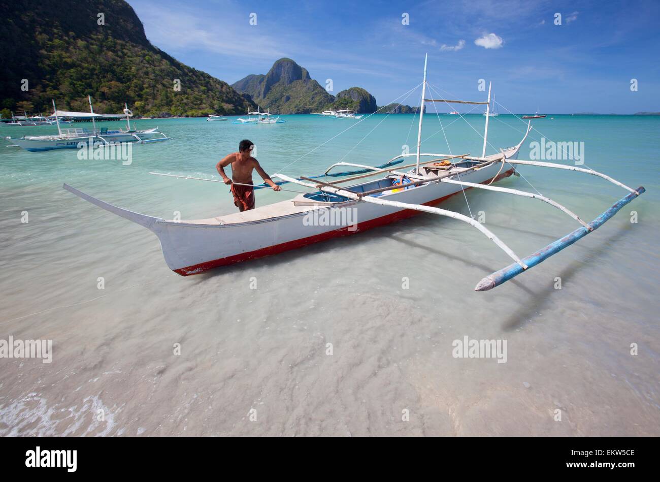 A Man Secures His Wooden Bangka Boat In The Bay; El Nido, Bacuit Archipelago, Palawan, Philippines Stock Photo