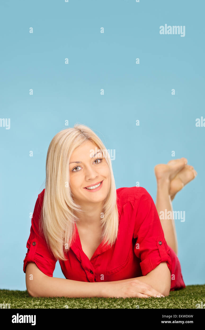Studio shot of young blond woman in a red dress lying on a grass ...