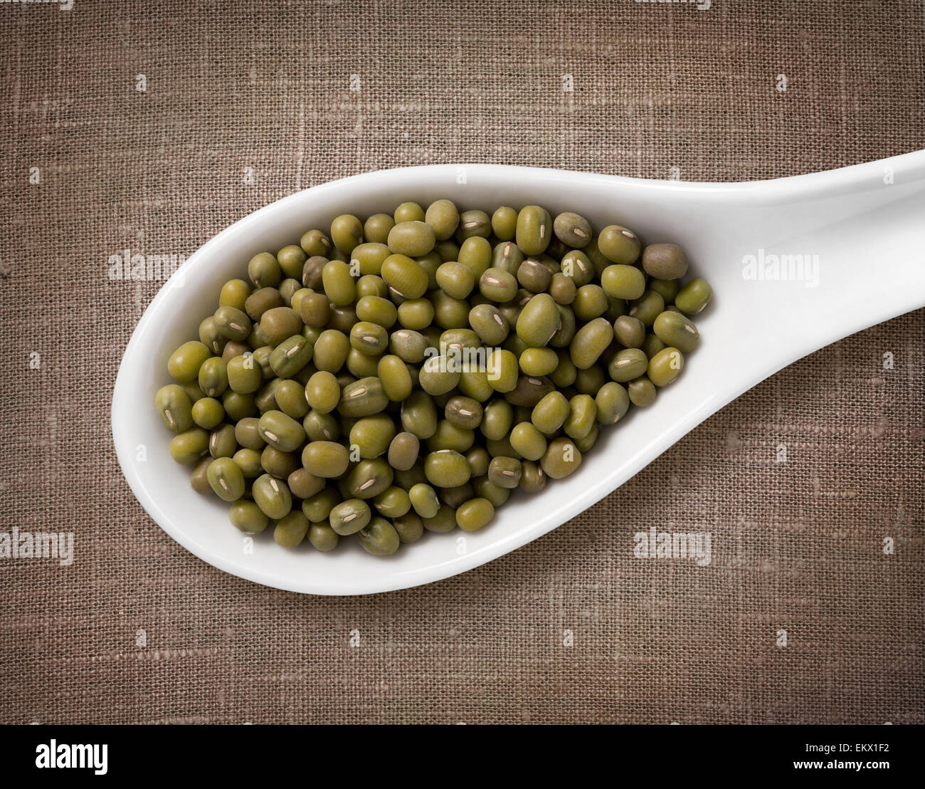 Mung beans in a wooden spoon / high-res photo of grain in white porcelain spoon on burlap sackcloth background Stock Photo