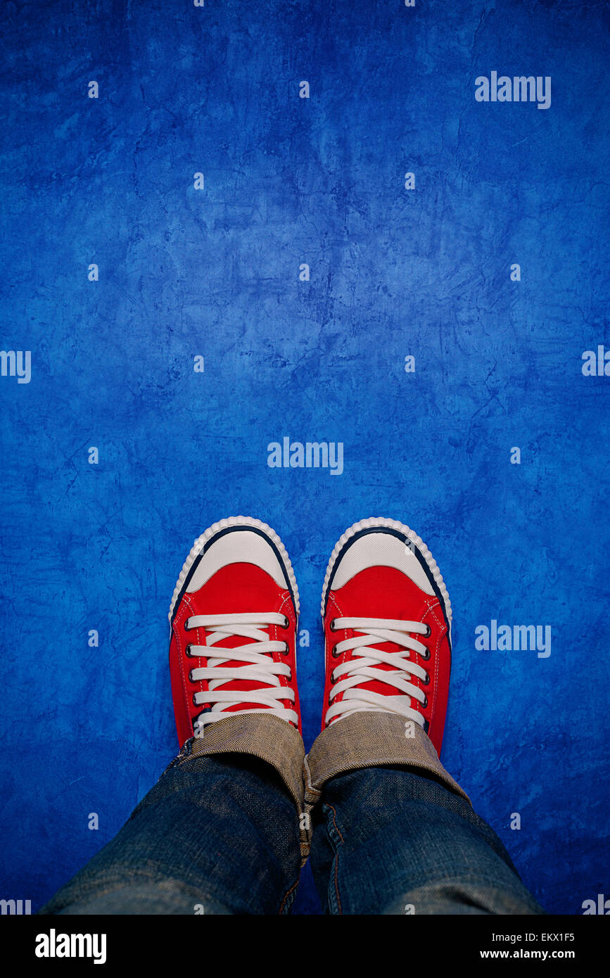Feet From Above Concept, Teenage Person in Red Sneakers Standing on Blue Background, Blank Copy Space in Front, Top View Stock Photo