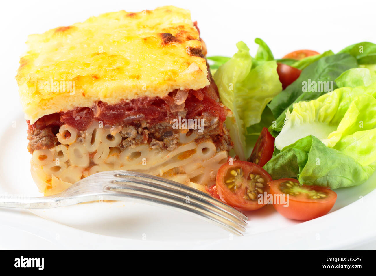 Greek pistatsio pasta topped with minced beef, tomatoes, bechamel sausce and cheese, served with a salad. Stock Photo