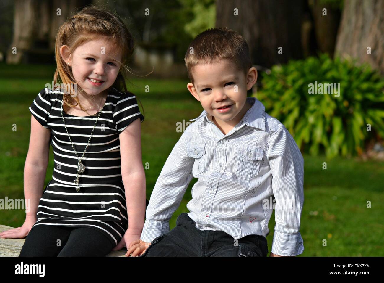 Brother and sister sitting and smiling in the park Stock Photo - Alamy