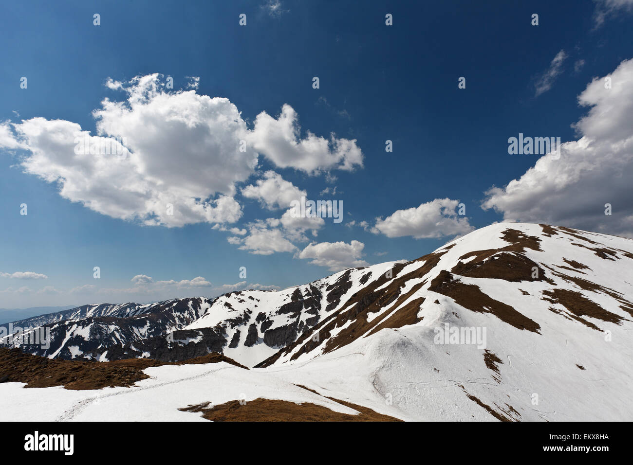 Sun and blue cloudy sky over spring Tatry mountains, covered with remnants of snow Stock Photo