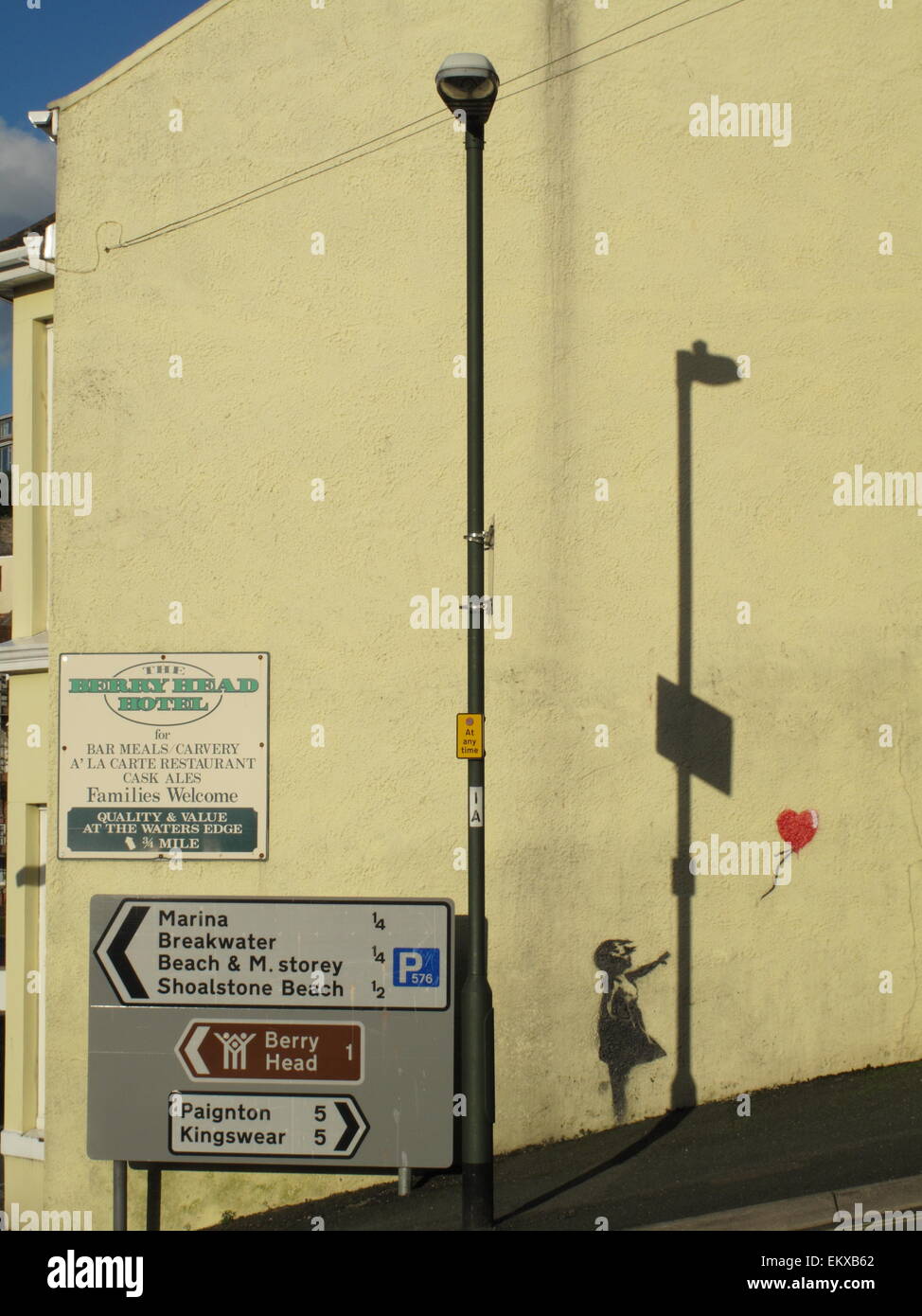 A Banksy mural of girl with red balloon on wall in Brixham Devon with shadows and street signs and Berry Head Hotel sign Stock Photo