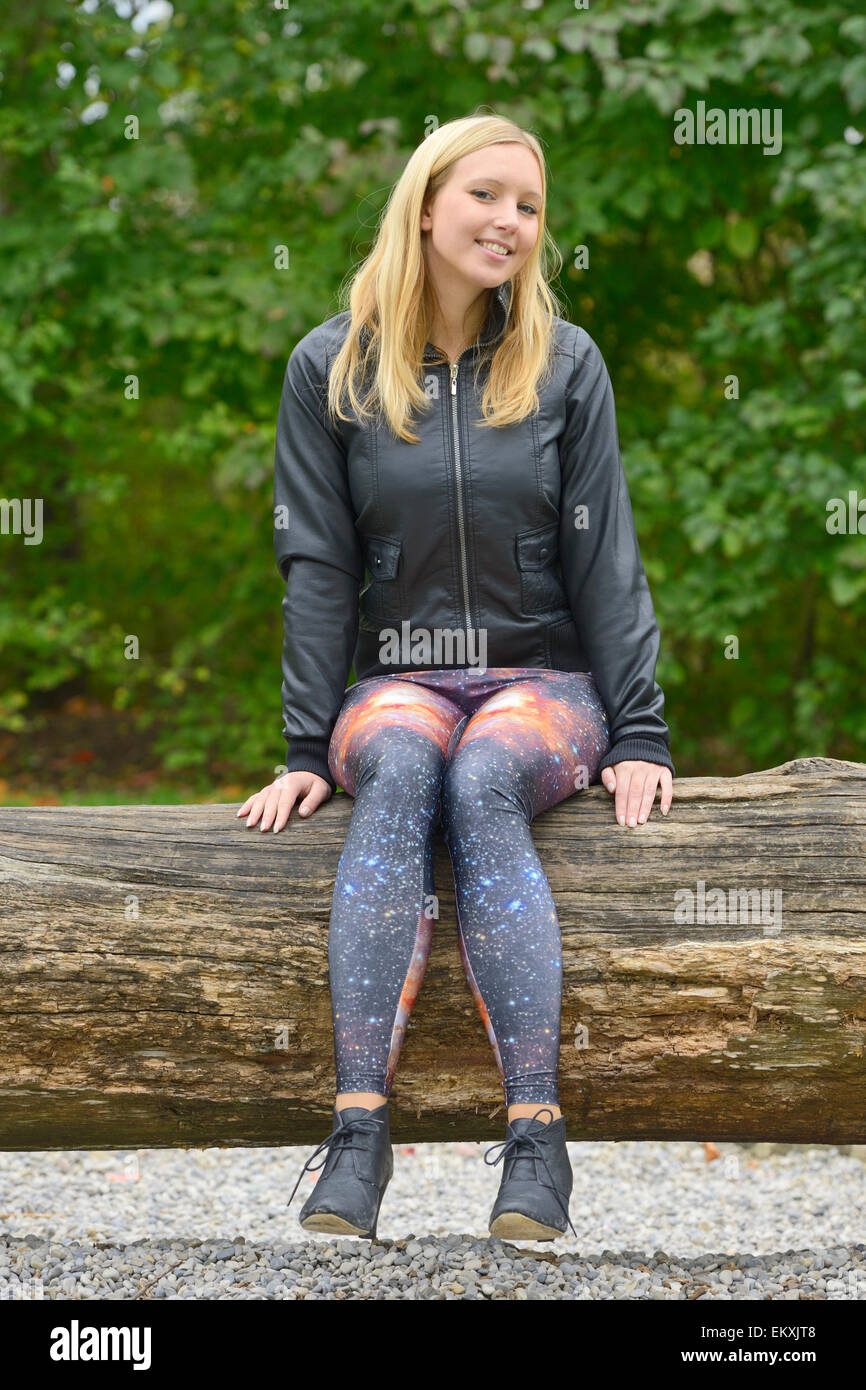 Attractive smiling young woman wearing fancy universe print leggings  sitting on a tree log Stock Photo - Alamy
